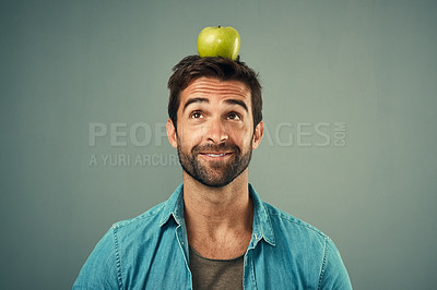 Buy stock photo Studio shot of a handsome young man posing with an apple on his head against a grey background