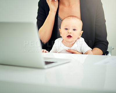 Buy stock photo Cropped shot of a businesswoman looking after her baby boy while working on her laptop