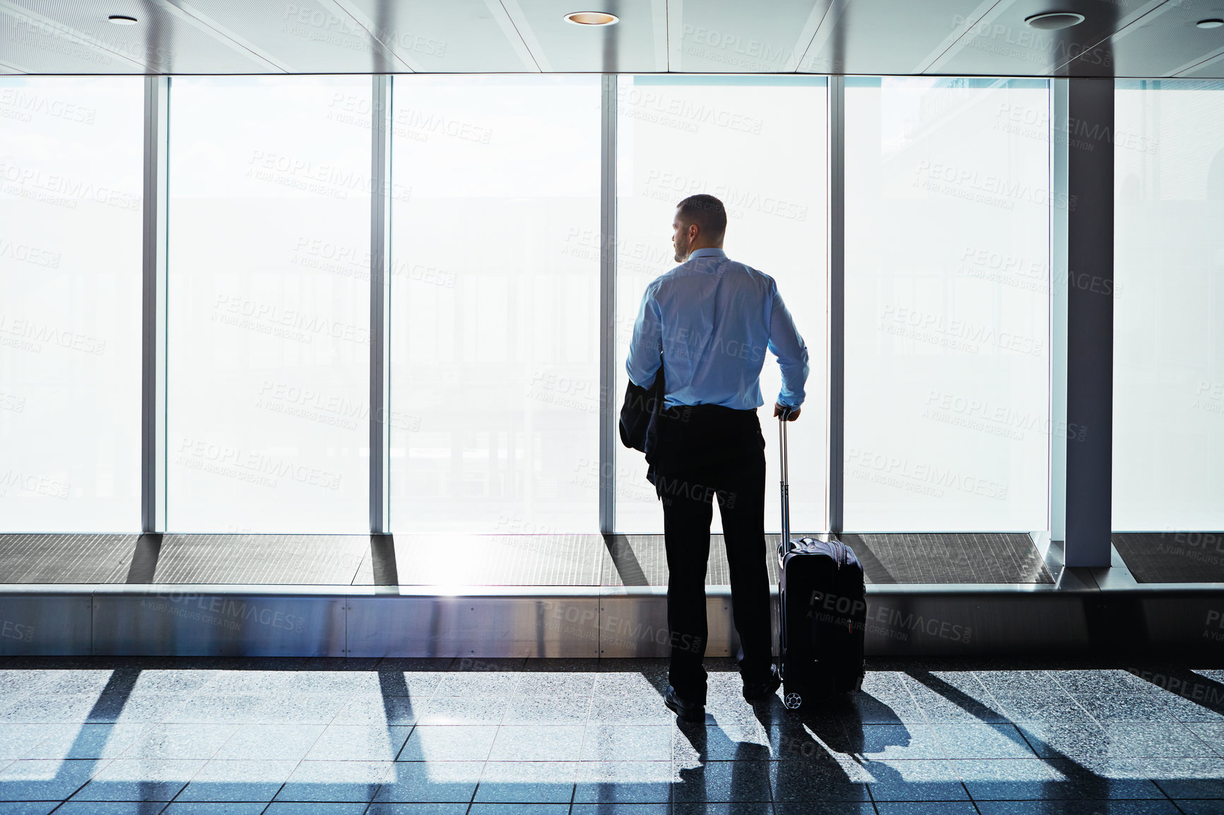 Buy stock photo Shot of a businessman looking through airport windows while on a business trip