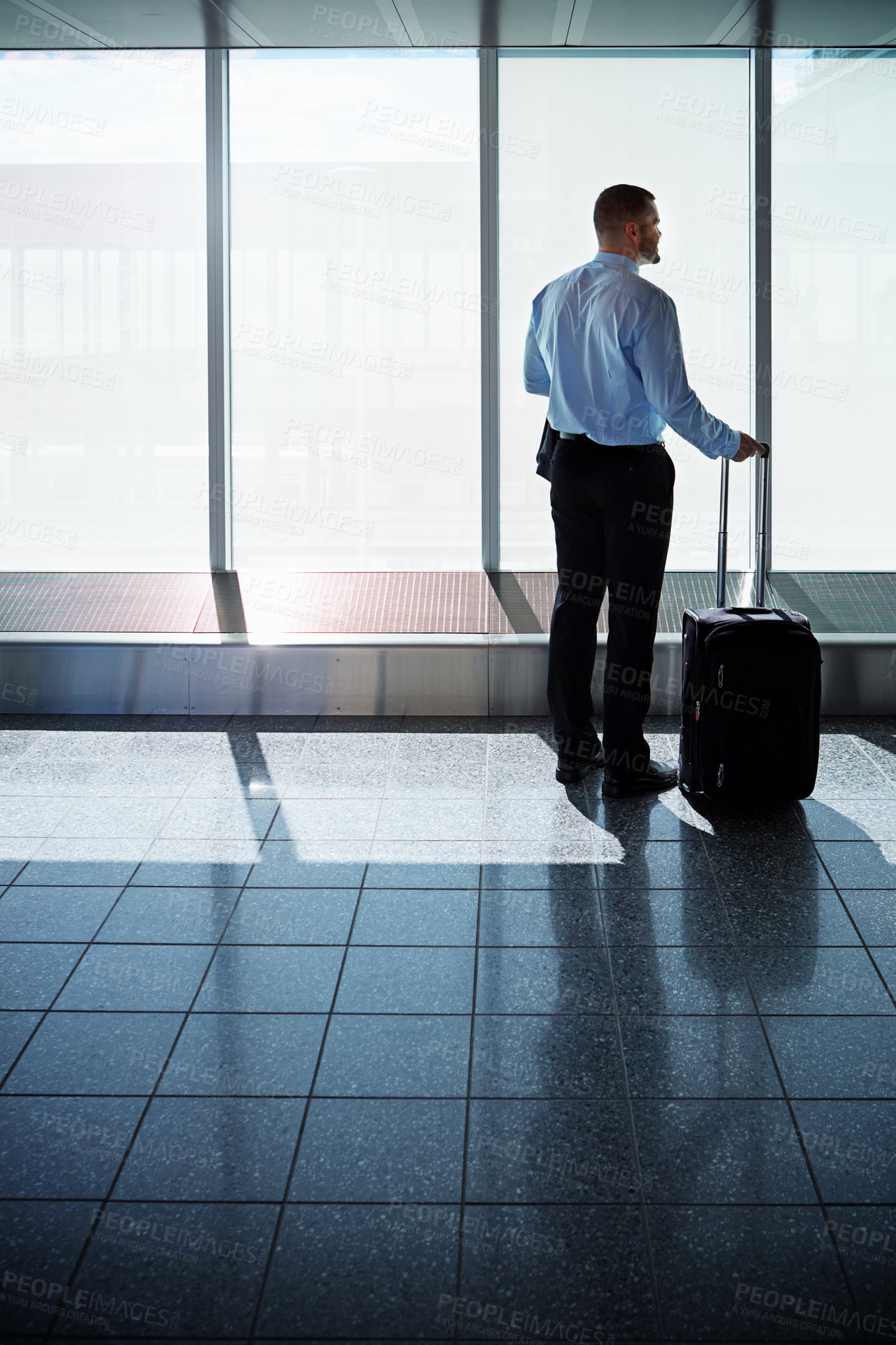 Buy stock photo Shot of a businessman looking through airport windows while on a business trip