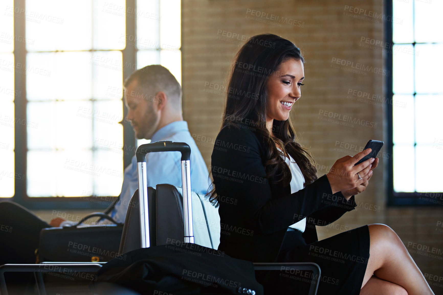 Buy stock photo Shot of two professional businesspeople using their smartphones while waiting in an airport terminal