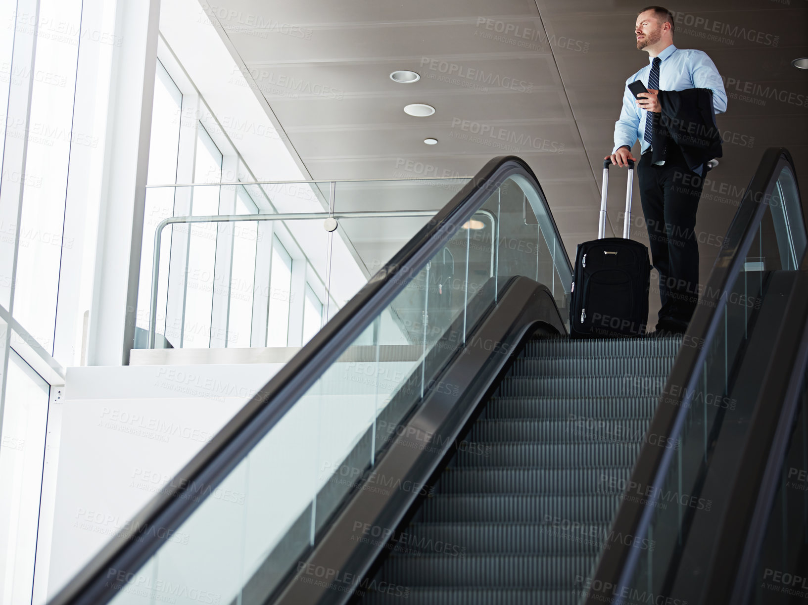 Buy stock photo Shot of a businessman traveling down an escalator in an airport