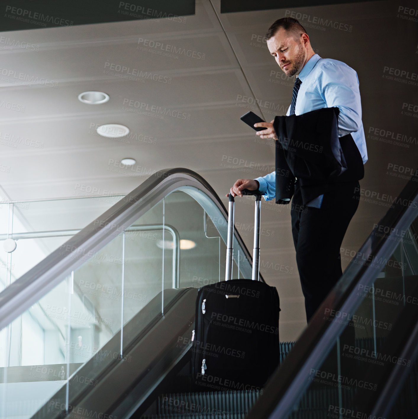 Buy stock photo Shot of a businessman using a mobile phone while traveling down an escalator in an airport