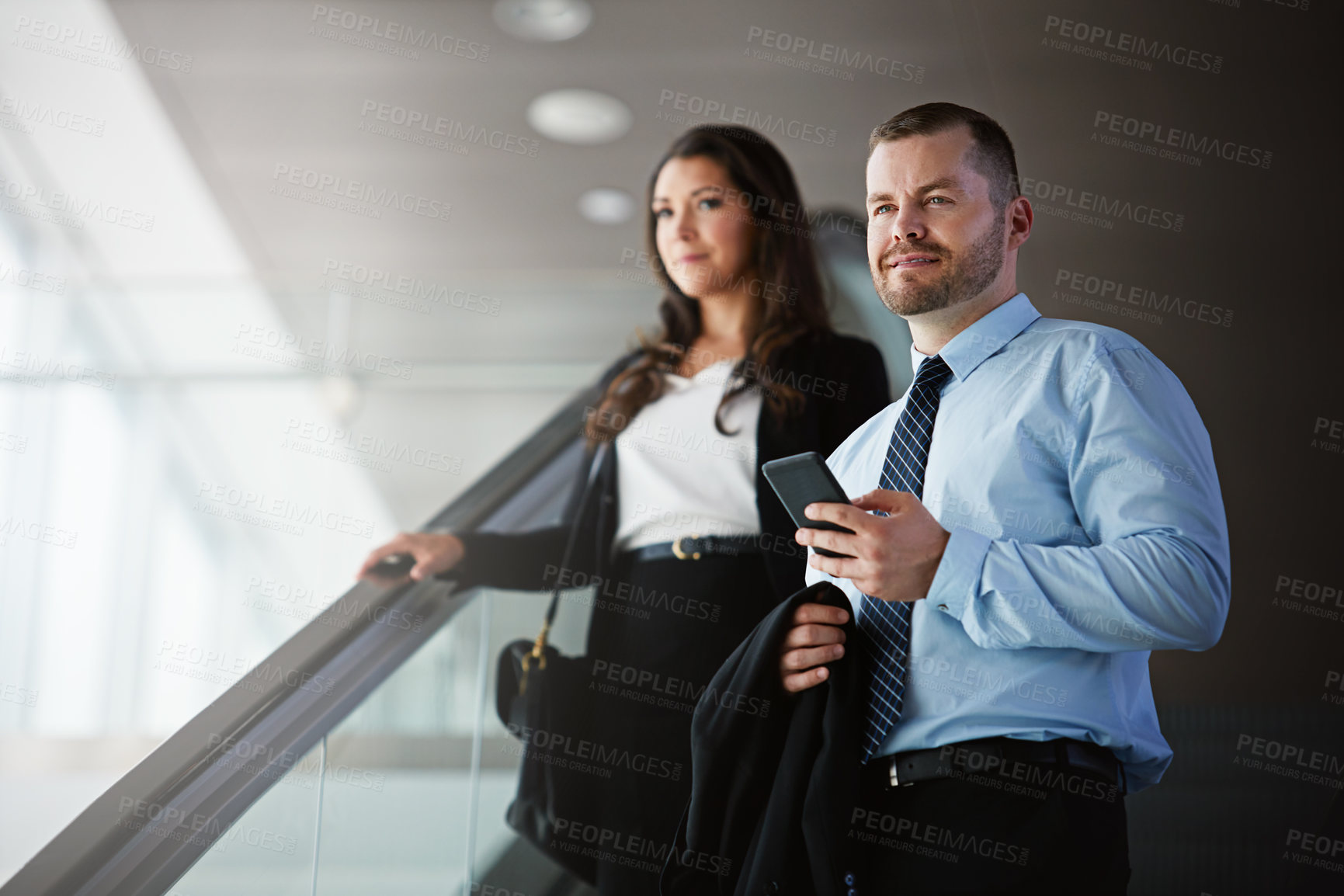 Buy stock photo Shot of a businessman and businesswoman traveling down an escalator in an airport