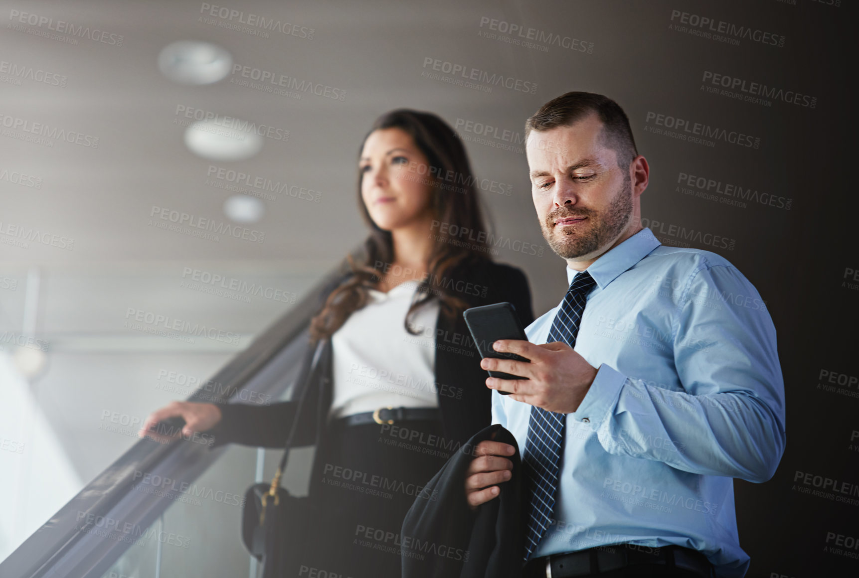 Buy stock photo Shot of a businessman using a mobile phone while traveling down an escalator in an airport