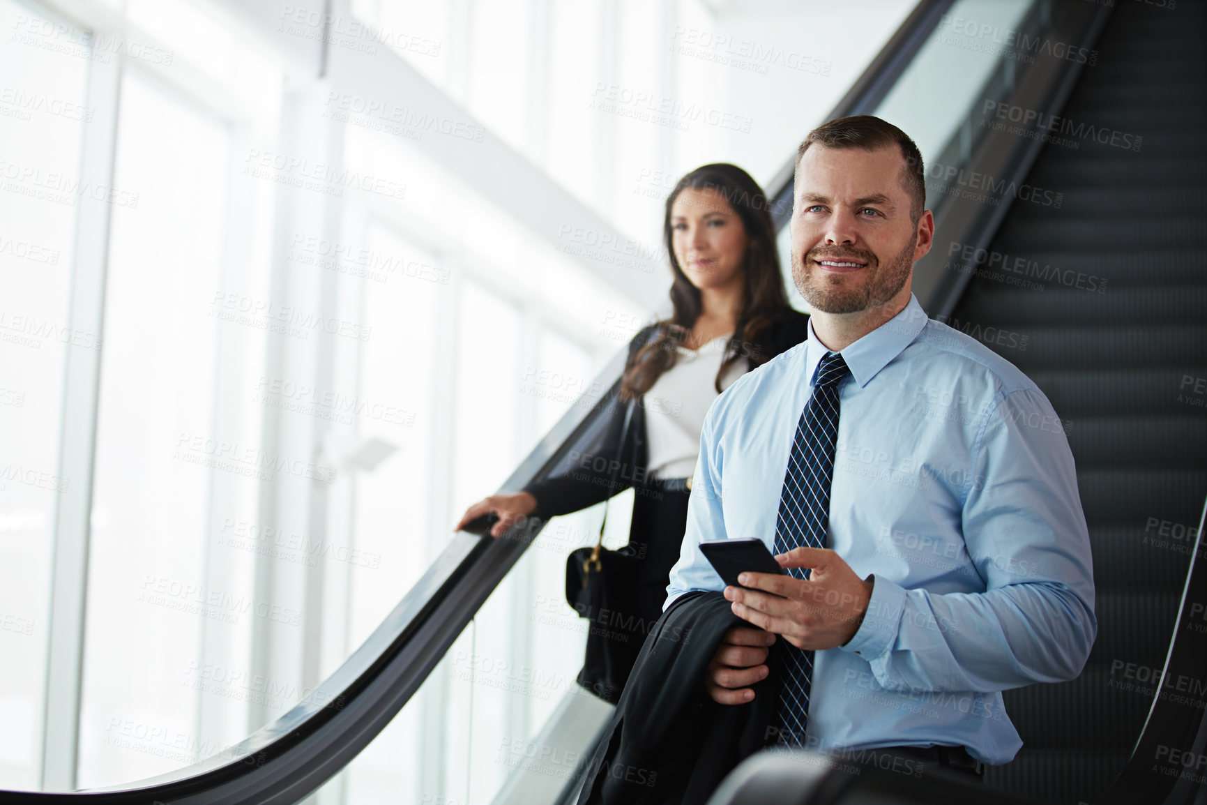 Buy stock photo Shot of a businessman and businesswoman traveling down an escalator in an airport