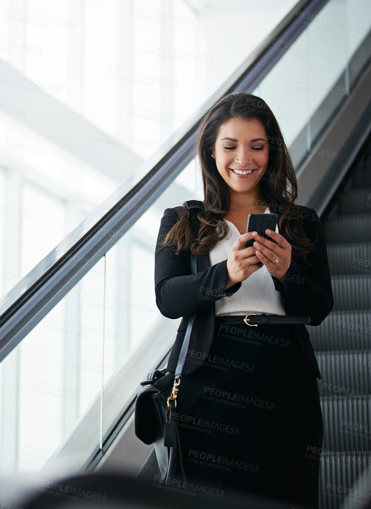 Buy stock photo Shot of a businesswoman using a mobile phone while traveling down an escalator in an airport