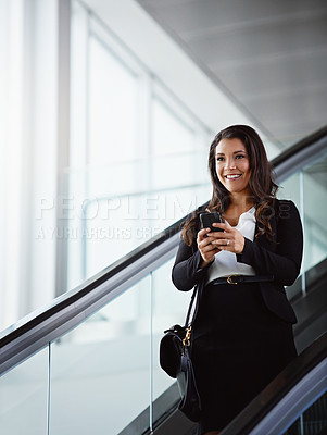 Buy stock photo Shot of a businesswoman using a mobile phone while traveling down an escalator in an airport