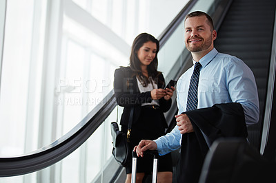 Buy stock photo Shot of a businessman traveling down an escalator in an airport with a businesswoman behind him
