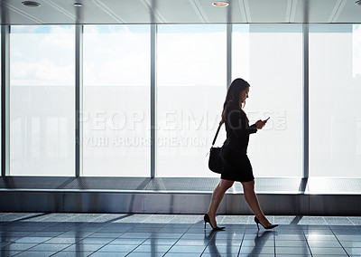Buy stock photo Shot of a businesswoman walking down an airport corridor using a cellphone while on a business trip