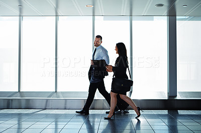Buy stock photo Shot of two businesspeople talking together while walking through an airport