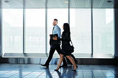 Buy stock photo Shot of two businesspeople talking together while walking through an airport