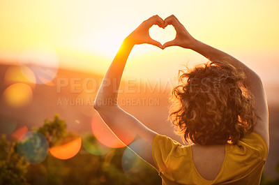Buy stock photo Rearview shot of an unidentifiable woman making a heart shape with her hands over a sunset landscape