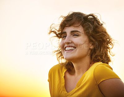 Buy stock photo Shot of a cheerful young woman smiling while standing outside at sunset
