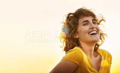 Buy stock photo Shot of a cheerful young woman laughing while standing outside at sunset