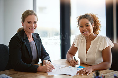 Buy stock photo Portrait of two smiling businesswoman sitting together at a table in an office