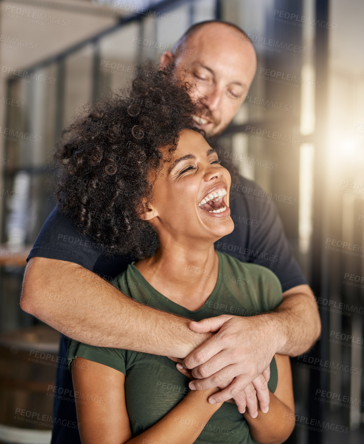 Buy stock photo Interracial couple, love hug and happy in home with security, bonding together and comedy conversation. Man, woman and smile for embrace with partnership, loyalty and laugh for funny chat or story