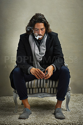 Buy stock photo Shot of a stylishly dressed man smoking an electronic cigarette while sitting in the studio