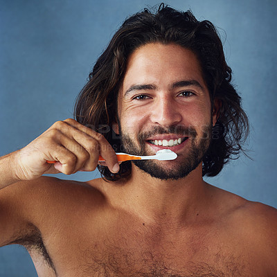 Buy stock photo Studio portrait of a handsome young man brushing his teeth against a blue background