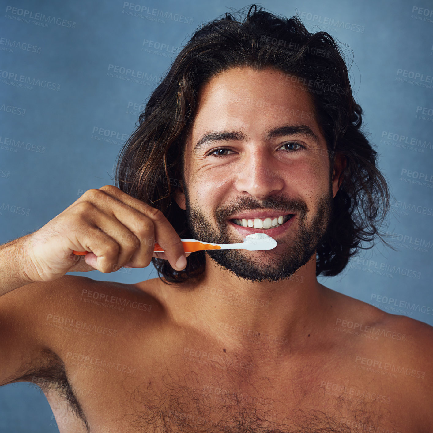 Buy stock photo Studio portrait of a handsome young man brushing his teeth against a blue background