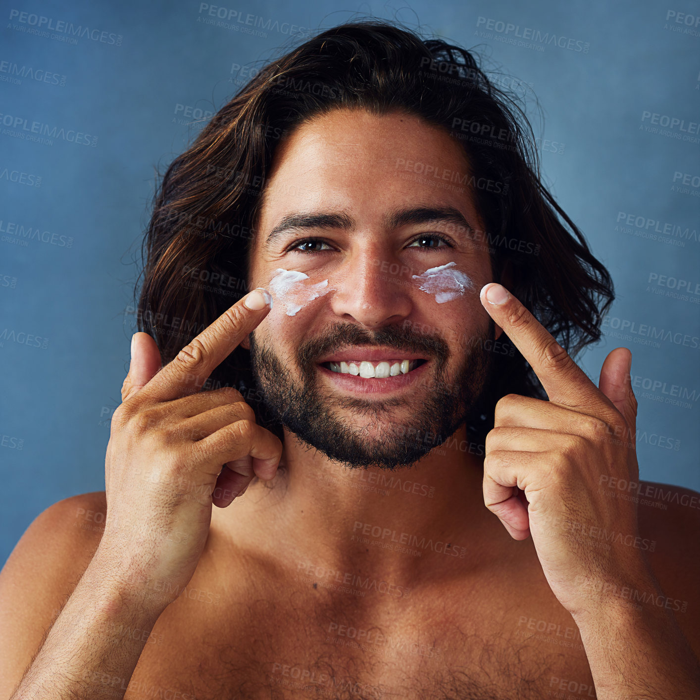 Buy stock photo Portrait, man and applying moisturizer in morning routine for wellness, skincare and hygiene on blue background. Male person, cosmetic and face product for healthy skin, confidence or pride in studio