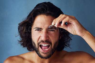 Buy stock photo Studio portrait of a handsome young man plucking his eyebrows against a blue background