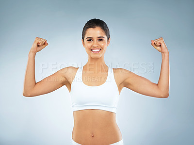 Buy stock photo Studio portrait of an attractive young woman flexing her muscles against a grey background
