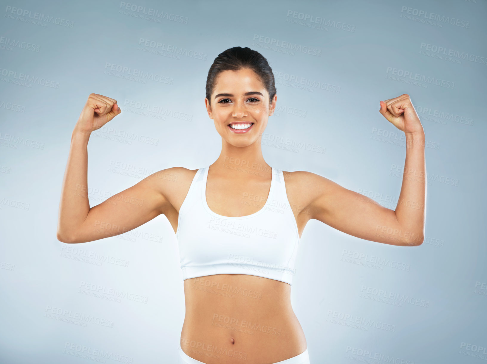 Buy stock photo Studio portrait of an attractive young woman flexing her muscles against a grey background
