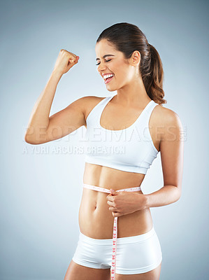 Buy stock photo Studio shot of an attractive young woman cheering while measuring her waist against a grey background
