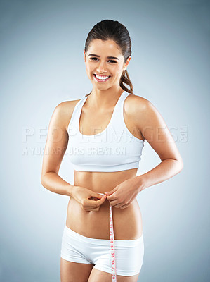 Buy stock photo Studio portrait of an attractive young woman measuring her waist against a grey background