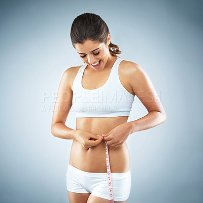Buy stock photo Studio shot of an attractive young woman measuring her waist against a grey background