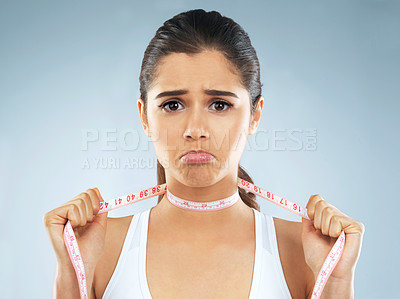 Buy stock photo Studio portrait of an attractive young woman with a measuring tape wrapped around her neck against a grey background