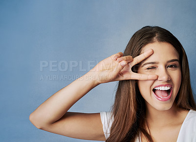 Buy stock photo Happy woman, portrait and face with peace sign for friendly, funky or positive attitude on a blue studio background. Female person, brunette or young model with smile or emoji for cool, fun or humor