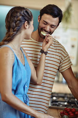 Buy stock photo Shot of an affectionate young couple snacking while preparing a meal in their kitchen