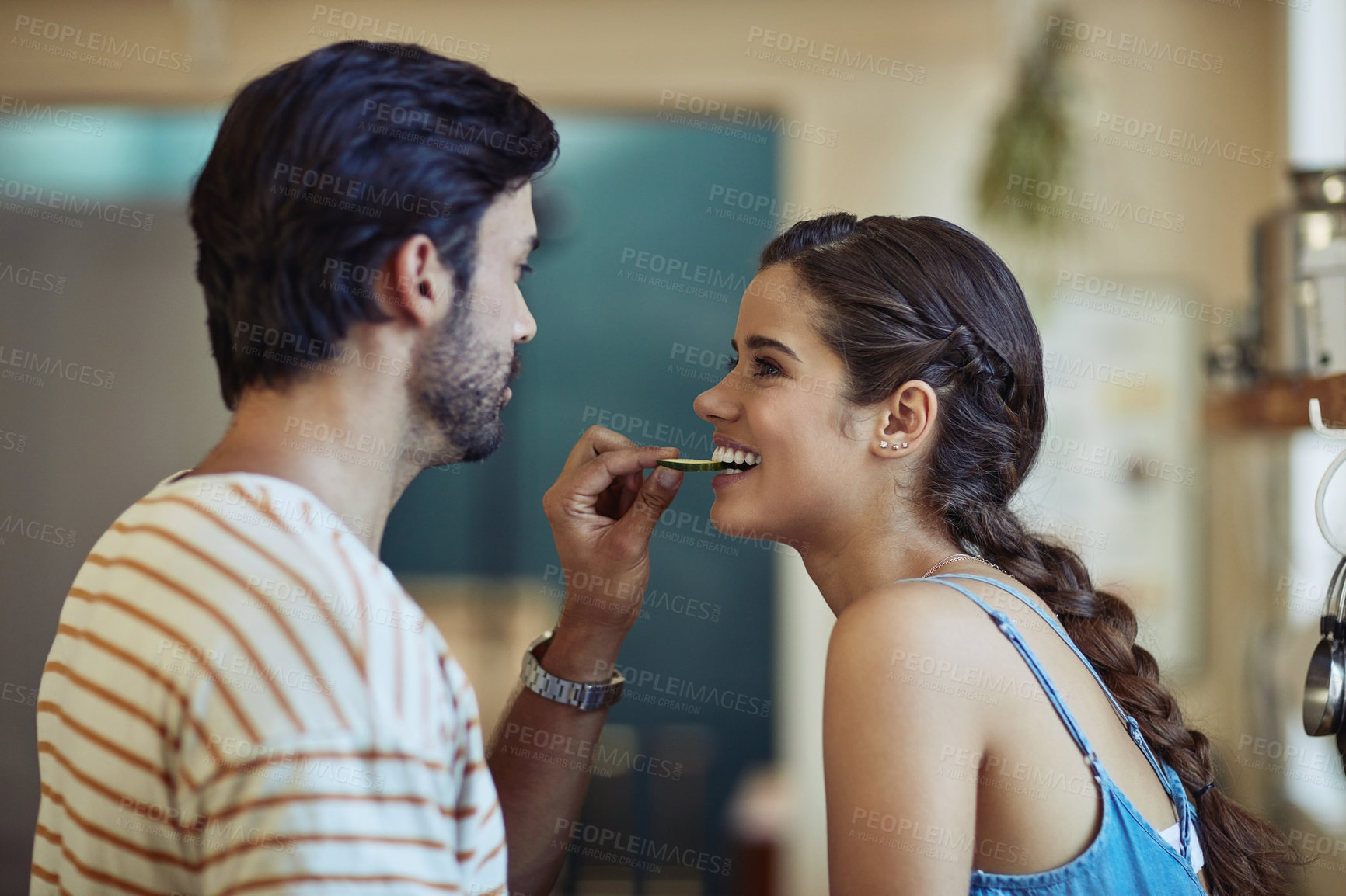 Buy stock photo Shot of an affectionate young couple snacking while preparing a meal in their kitchen