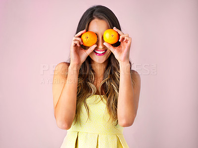 Buy stock photo Studio shot of a young woman holding up oranges in front of her eyes