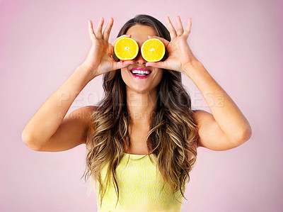 Buy stock photo Studio shot of a young woman holding up two halves of a orange in front of her eyes