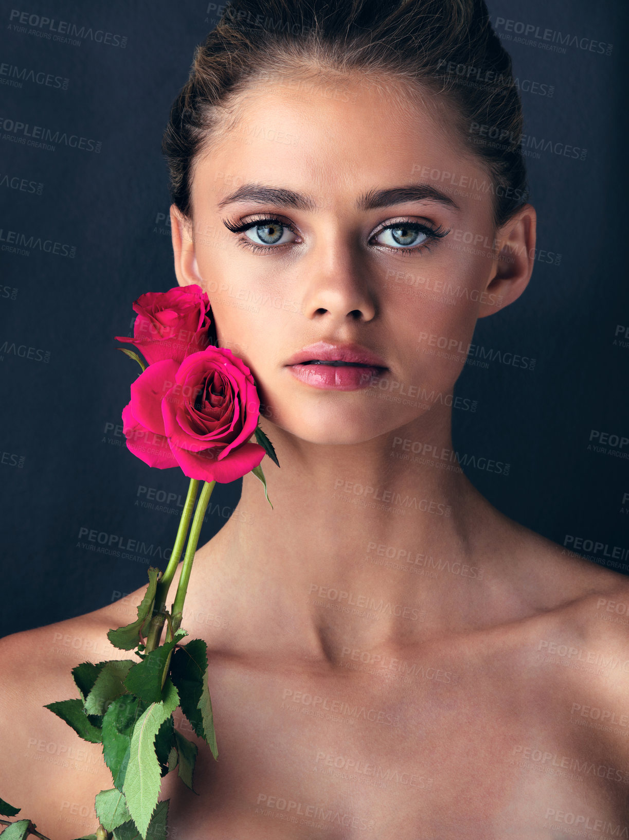 Buy stock photo Studio shot of an attractive young woman posing next to a couple of beautiful pink roses