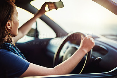 Buy stock photo Cropped shot of a young woman adjusting the rearview mirror in her car