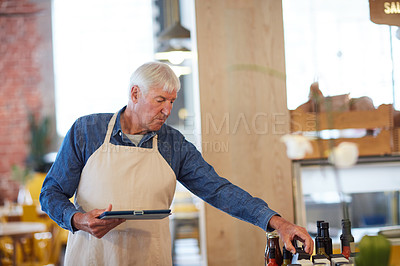 Buy stock photo Shot of a happy senior business owner using a tablet in his coffee shop