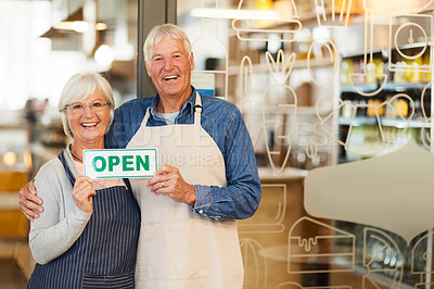 Buy stock photo Portrait of two happy senior business owners holding an open sign while standing inside their coffee shop