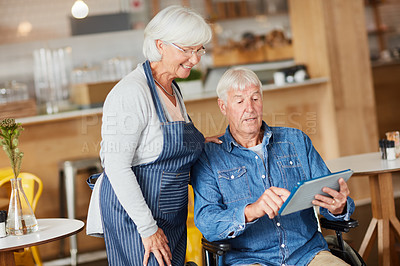 Buy stock photo Shot of two senior business owners looking at a tablet together while working in their coffee shop