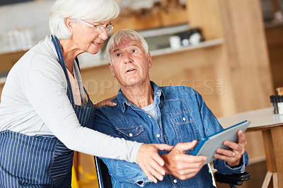 Buy stock photo Shot of two senior business owners looking at a tablet together while working in their coffee shop