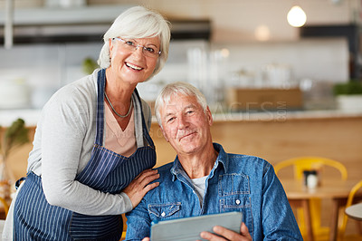 Buy stock photo Portrait of two senior business owners looking at a tablet together while working in their coffee shop
