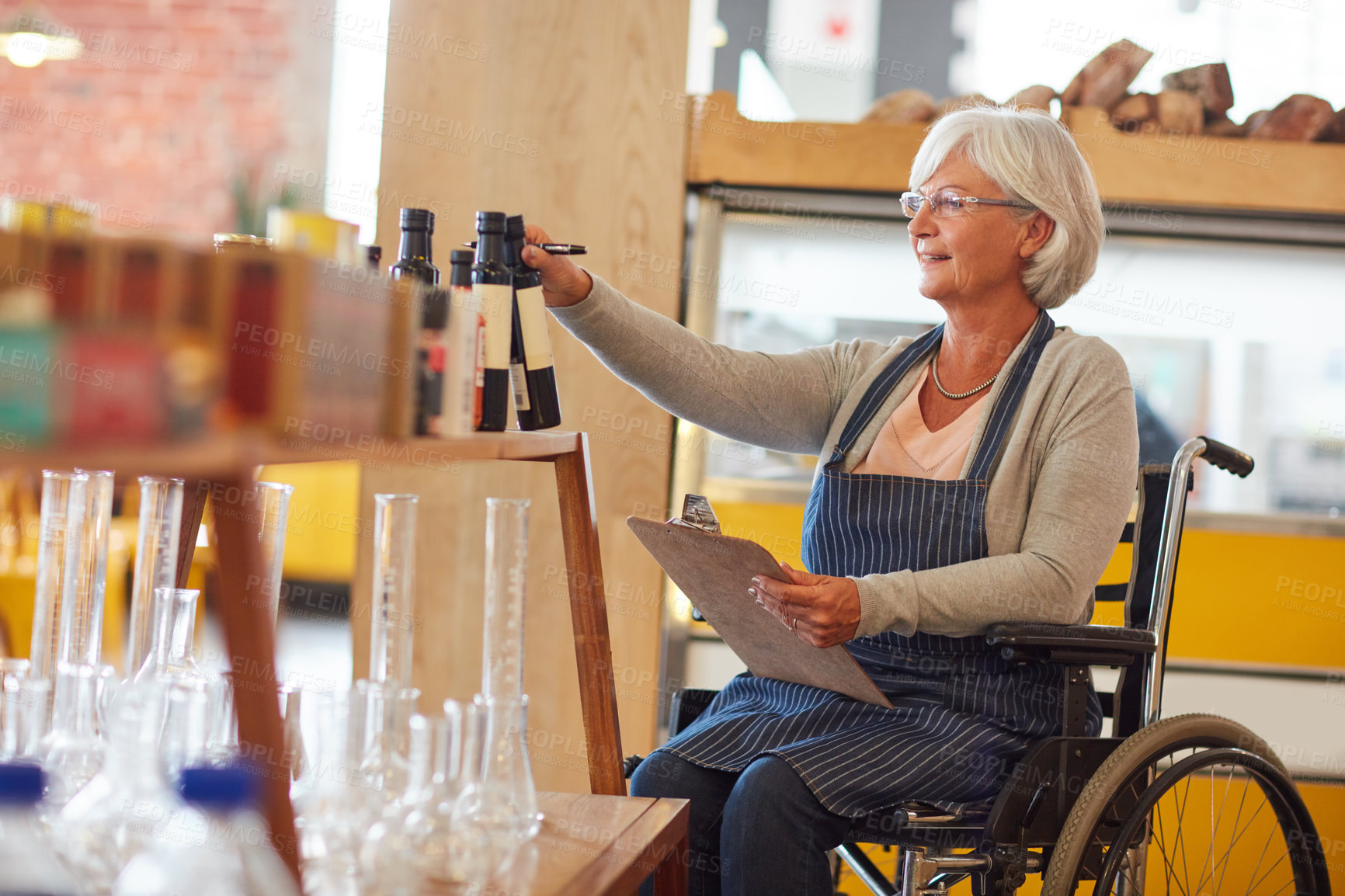 Buy stock photo Shot of a senior woman in a wheelchair doing stock take in her coffee shop