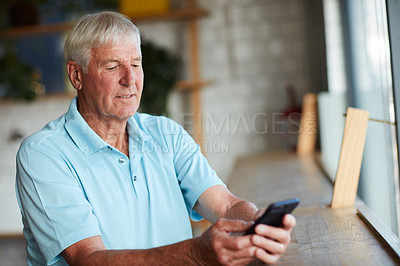 Buy stock photo Cropped shot of a senior man using his cellphone while sitting in a coffee shop