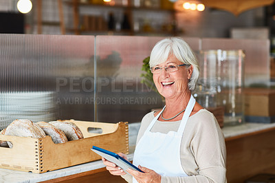 Buy stock photo Shot of a happy senior woman using a digital tablet to manage her bakery