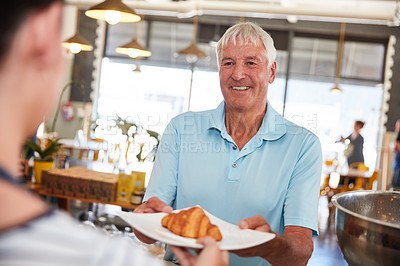 Buy stock photo Shot of a happy senior man being served a croissant in a cafe