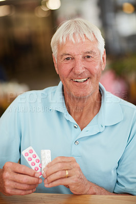 Buy stock photo Cropped shot of a senior man holding up his medication while sitting in a cafe