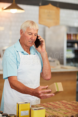 Buy stock photo Shot of a senior man talking on the phone while looking at merchandise in his cafe